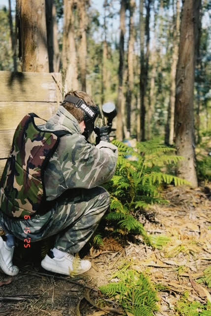 Jogador de paintball agachado atrás de bunker numa floresta de eucaliptos